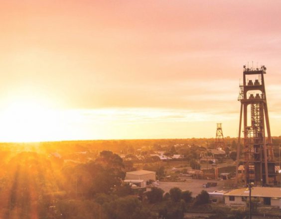 A panoramic view of Kalgoorlie, with the sunset shining over the town's buildings, trees, and mining architecture